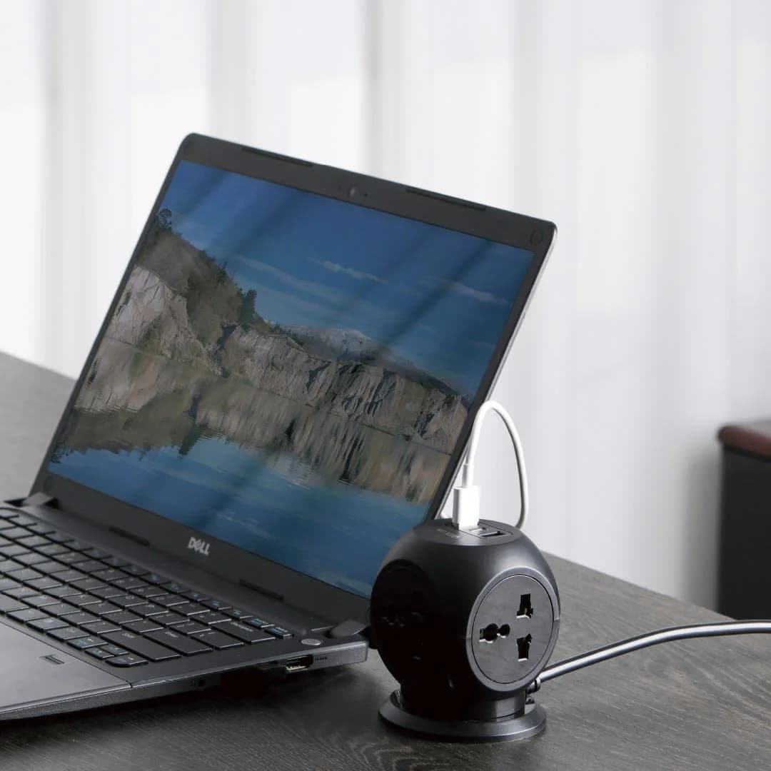 چندراهی Green Lion MultiPort Desk روی میز کنار یک لپ‌تاپ؛ کابل USB-C سفید به پورت بالای دستگاه وصل شده و کابل برق از کنار بیرون آمده است